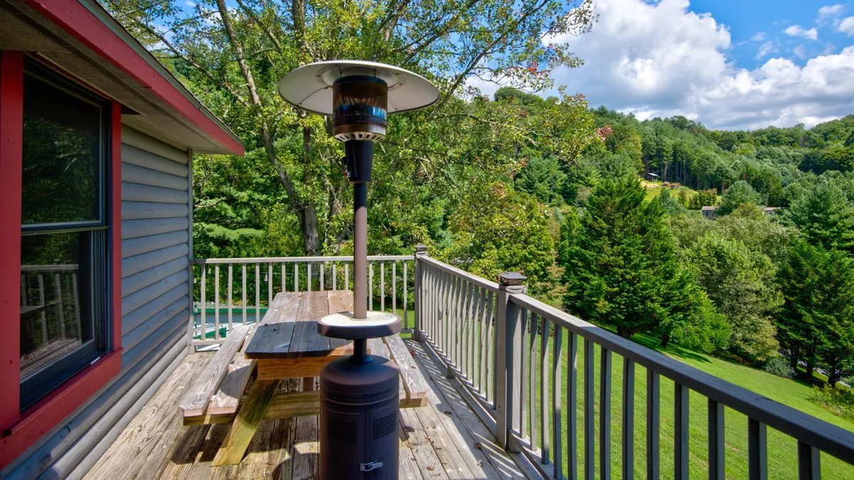 This image showcases a wooden deck with a patio heater, a picnic table, and lush green landscape beyond the deck railing. The setup is perfect for outdoor dining and gathering, with the heater suggesting comfort in cooler mountain evenings.