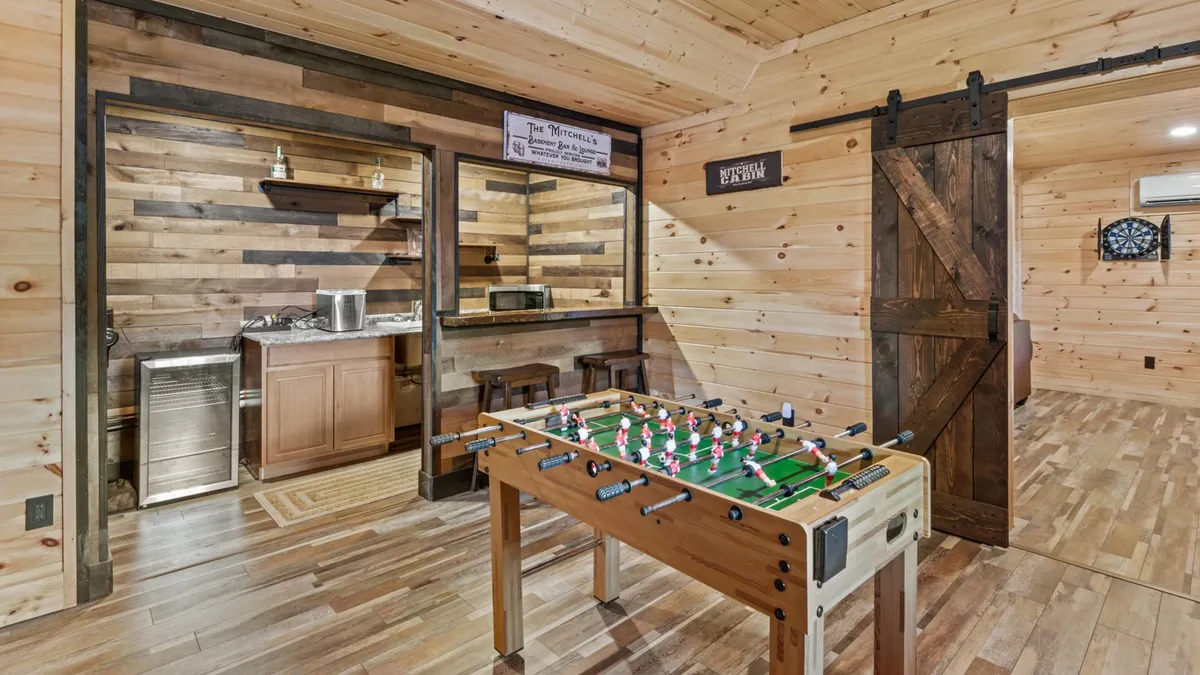 An indoor game room scene showing a foosball table and a bar area, all with cozy wooden walls. The room evokes a sense of fun and togetherness, hinting at lively family game nights or relaxed downtime after a day out.