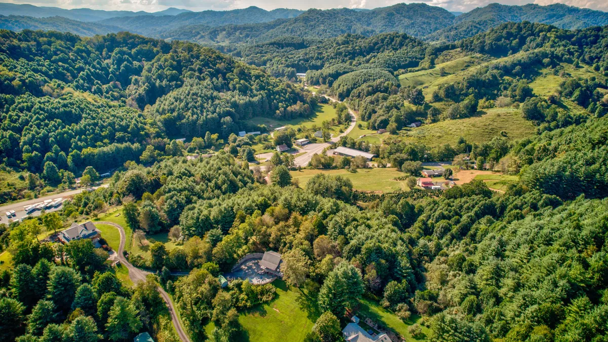 A sweeping view of rolling hills, dense forests, and a small mountain community nestled among the trees. The image evokes a sense of adventure and the beauty of the High Country, inviting travelers to explore the outdoors.