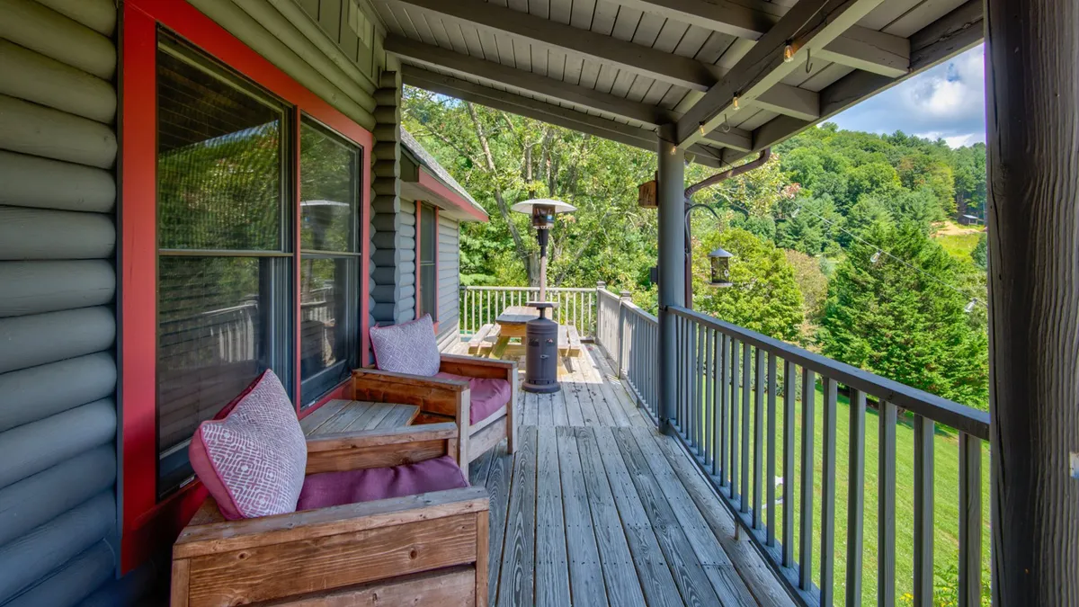 This exterior image features a spacious wooden deck with comfortable cushioned chairs, a table, and an outdoor heater, all set against a lush backdrop of greenery. The inviting setup encourages relaxation and socialization while enjoying the tranquil mountain setting.