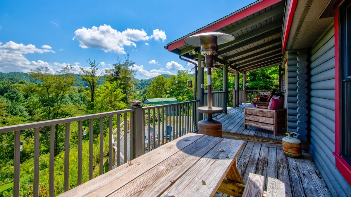This image showcases an expansive deck set against a backdrop of lush trees and distant mountain views. The deck features outdoor seating and an outdoor heater, inviting guests to relax while taking in the panoramic scenery. The space is ideal for unwinding after adventures, sharing meals, or stargazing at night.