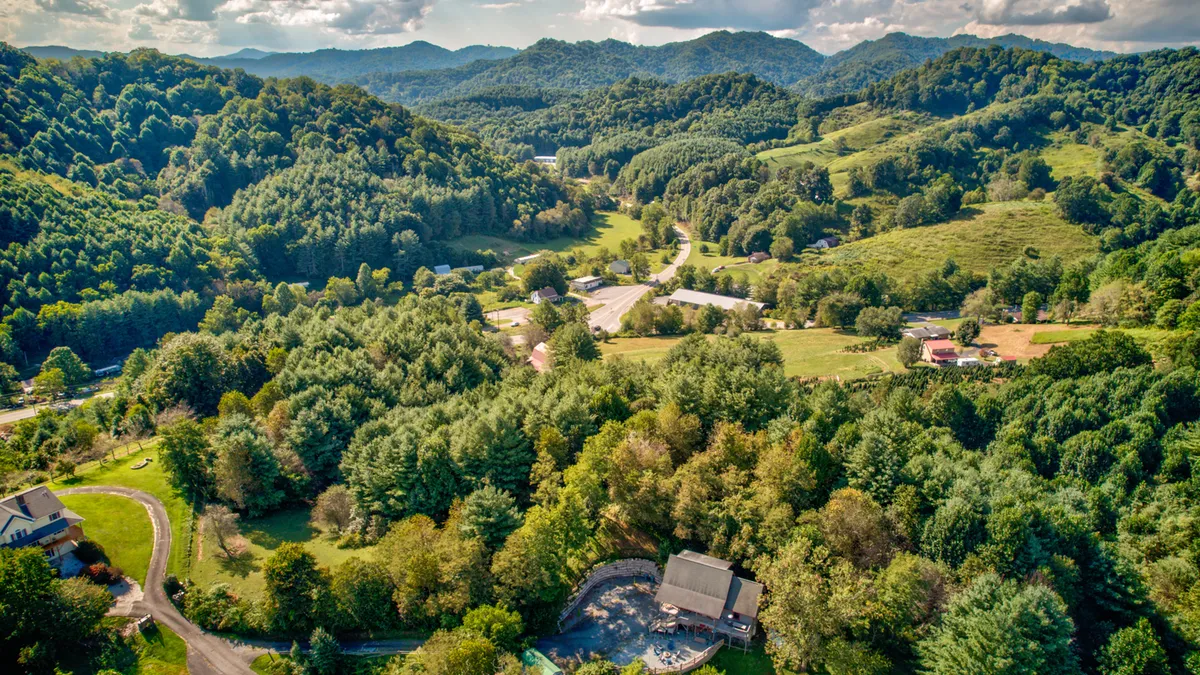 A sweeping view of rolling hills, forests, and a meandering road, with hints of local amenities like a swimming pool. The scenery evokes the adventure and natural beauty of the Blue Ridge area, encouraging outdoor exploration.