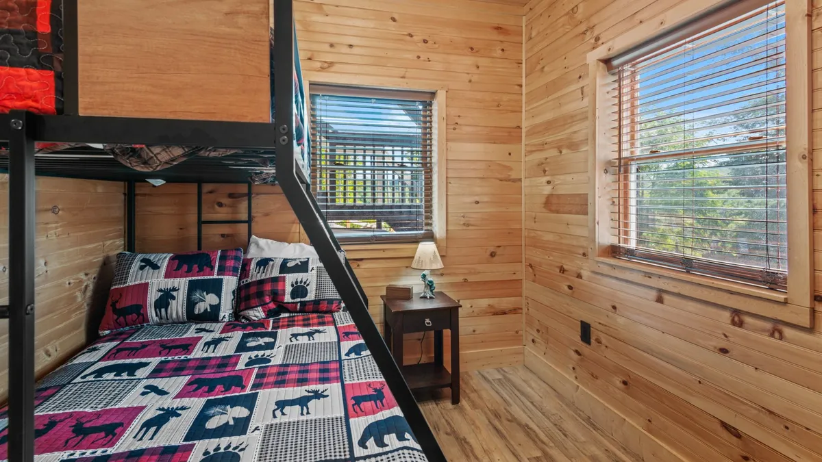 A lower-level bunk room designed for kids or teens, with a sturdy bunk bed, colorful bedding, a nightstand with lamp, and wood accents. The playful yet inviting atmosphere makes it ideal for younger guests or families.