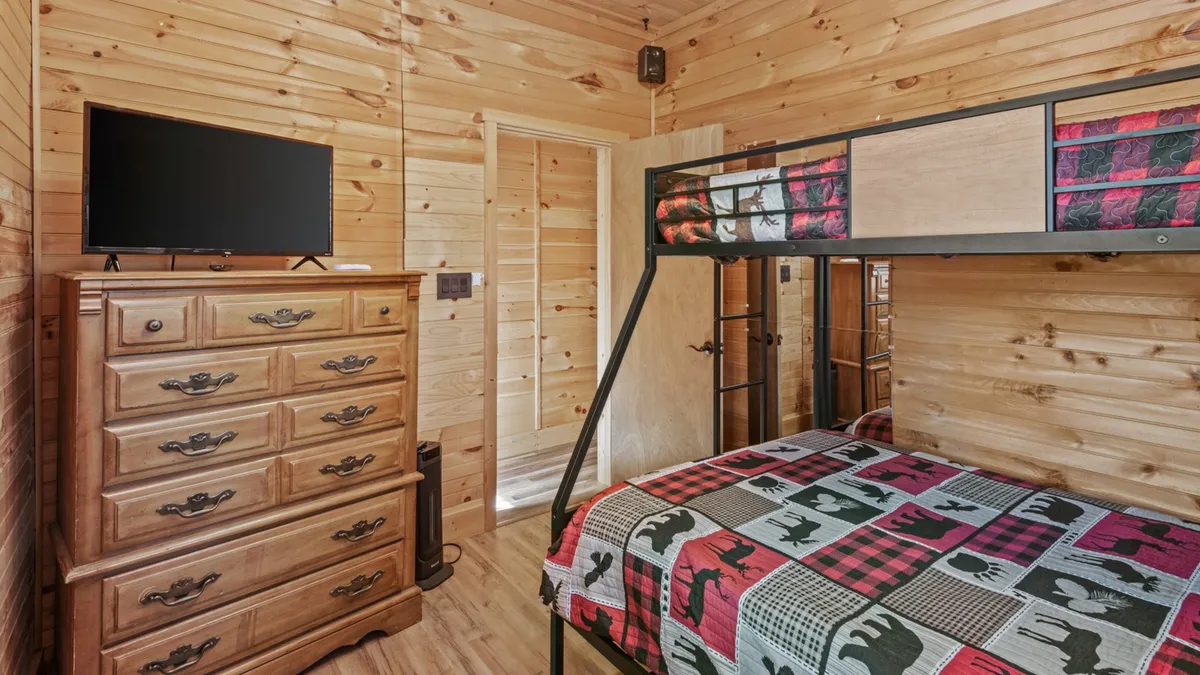 A cozy bunk room with a sturdy bunk bed, dresser, and television, designed for kids or young guests to relax, watch TV, or have fun sleepovers. The decor is warm and inviting, ideal for families with children.